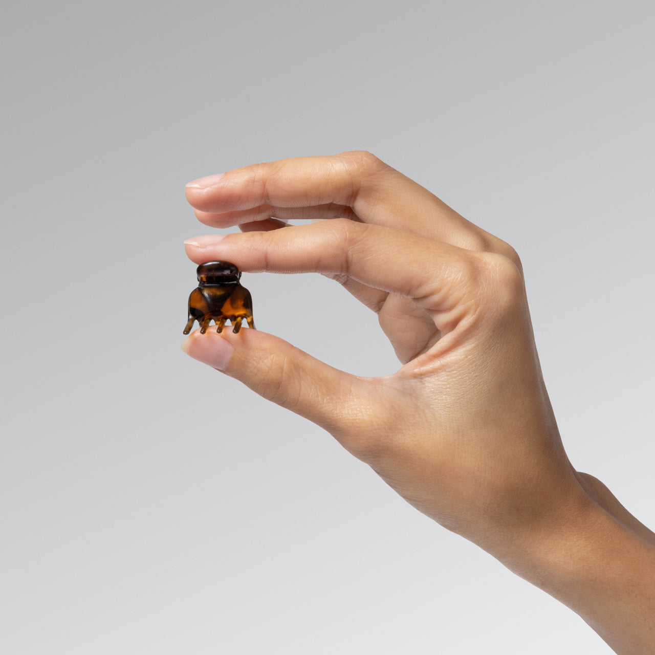 Hand holding a kitsch Tort Micro Cloud Clip between 2 fingers against a plain background