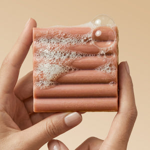 Close-up of hand holding Kitsch Amber Shores Body Wash Bar with rich sudsy lather and bubbles