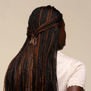Person with mirco braids styled in a mini gold claw clip against a neutral background