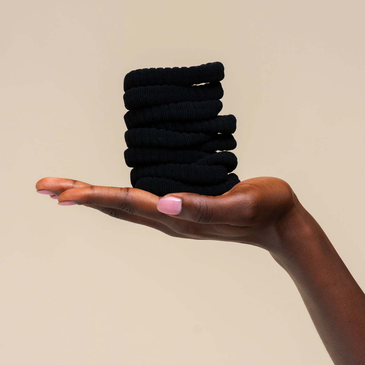 Hand holding a stack of kitsch ribbed black hair ties against a beige background