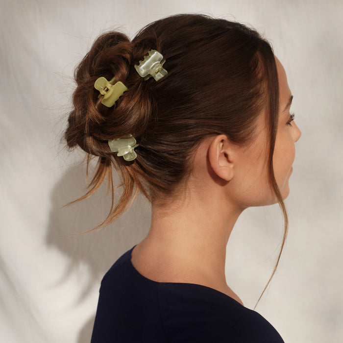 Female model with dark brown messy updo wearing multiple KITSCH Pearlized Cream & Butter Yellow Jelly Cloud Clips Mini — side/back profile view, dark navy top, white background — butter yellow & pearlized cream mini claw clips styling the updo — All-Day Hold | 8pcs, Made from Recycled Materials