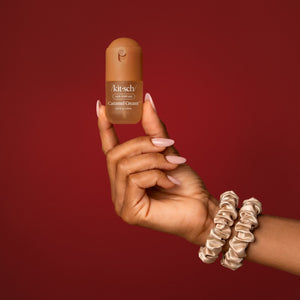KITSCH Sweet & Silky Hair 4pc Set — model's hand with light pink nails holding the Caramel Cream mini hair perfume, two champagne satin scrunchies worn on the wrist, deep red backdrop — travel-friendly bottles — spritz on your hair, body, and even your Kitsch Satin Pillowcase