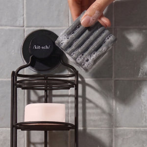 KITSCH Charcoal Detoxifying Solid Body Wash — hand lifting the lathered charcoal bar from a Kitsch shower caddy on a tiled wall — Eco-friendly bar format reduces single-use plastic — keeping the bar in the shower