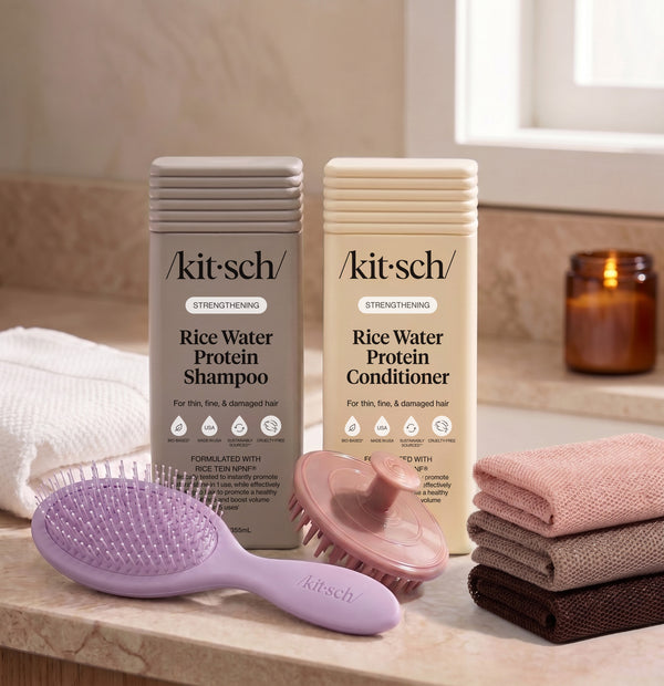 Kitsch Rice Water Protein Shampoo and Conditioner bottles on a bathroom counter, with a free soft violet wet/dry brush, a terracotta scalp exfoliator, and the rosewood net sponge as a free welcome kit.